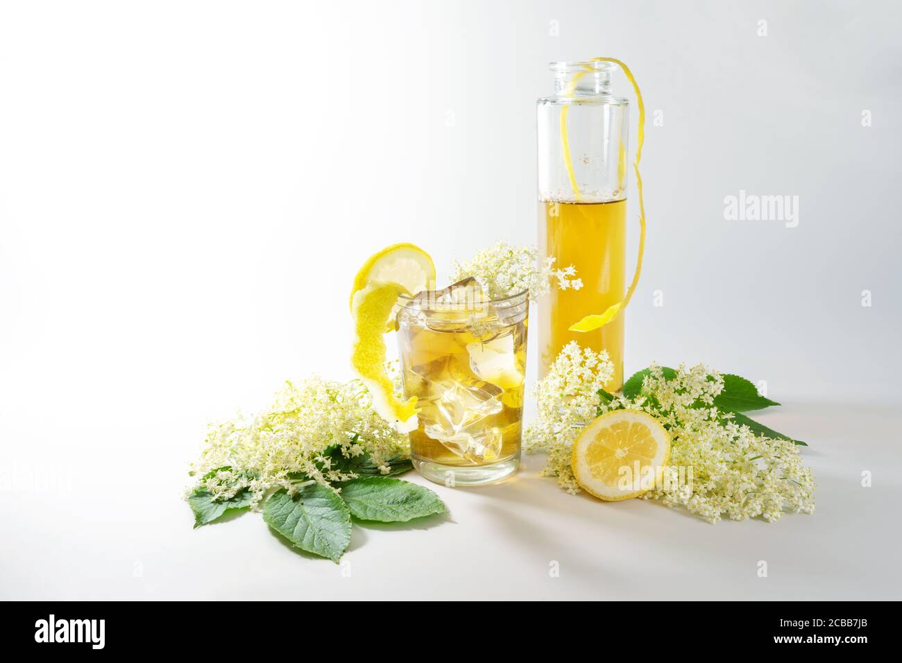 Sciroppo di fiori di sambuco in bottiglia e limonata fatta in casa con  cubetti di ghiaccio in un bicchiere da bere, scorza di limone e fette e  alcuni fiori freschi su una