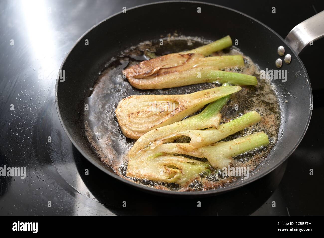 Verdure di finocchio saltate in burro marrone in una padella da cucina su una stufa nera, pasto vegetariano fatto in casa, spazio copia, fuoco selezionato Foto Stock
