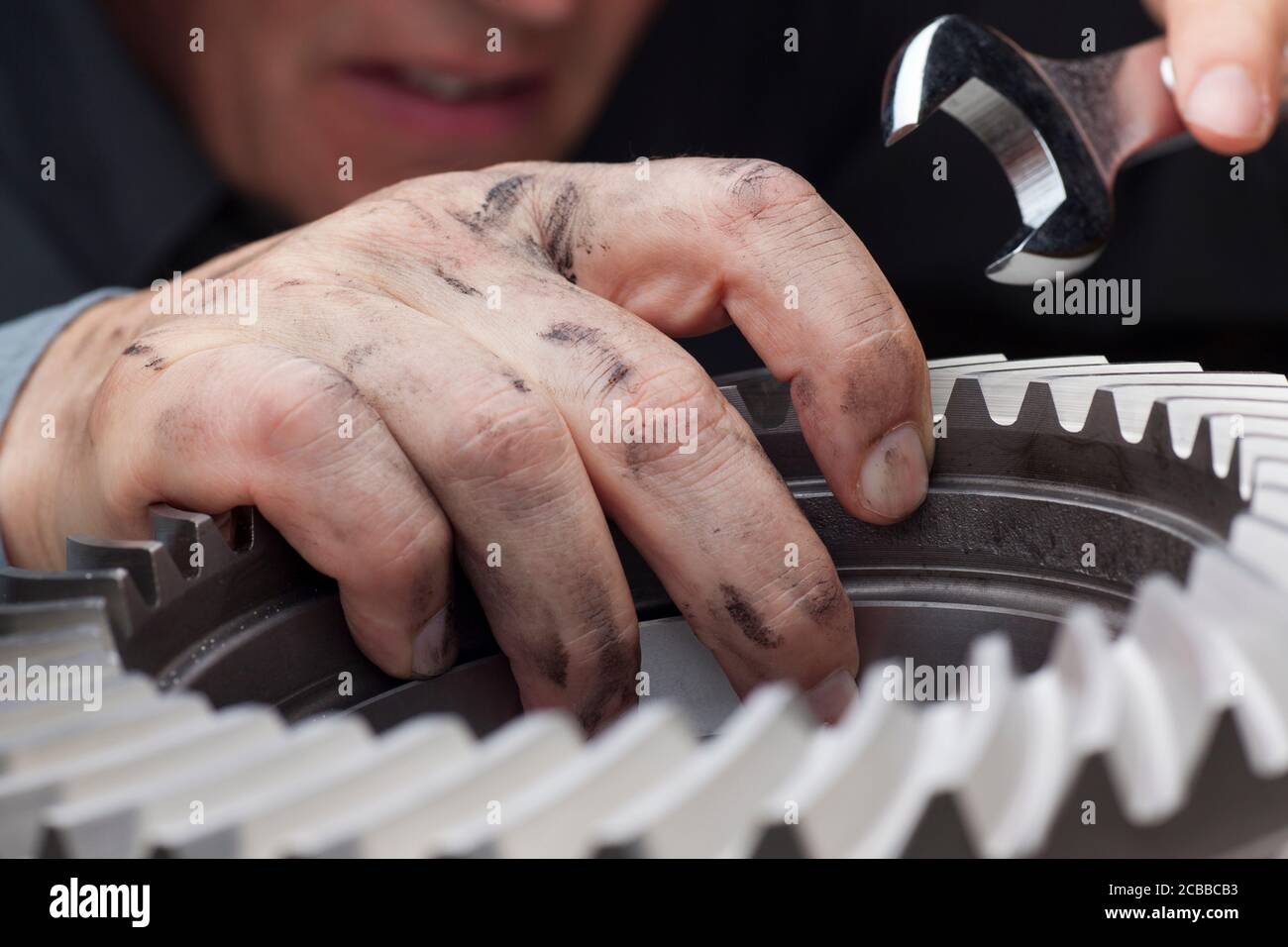 Riparatore con mani sporche lavorando con una chiave e un ruota dentata - messa a fuoco selettiva sulla mano Foto Stock