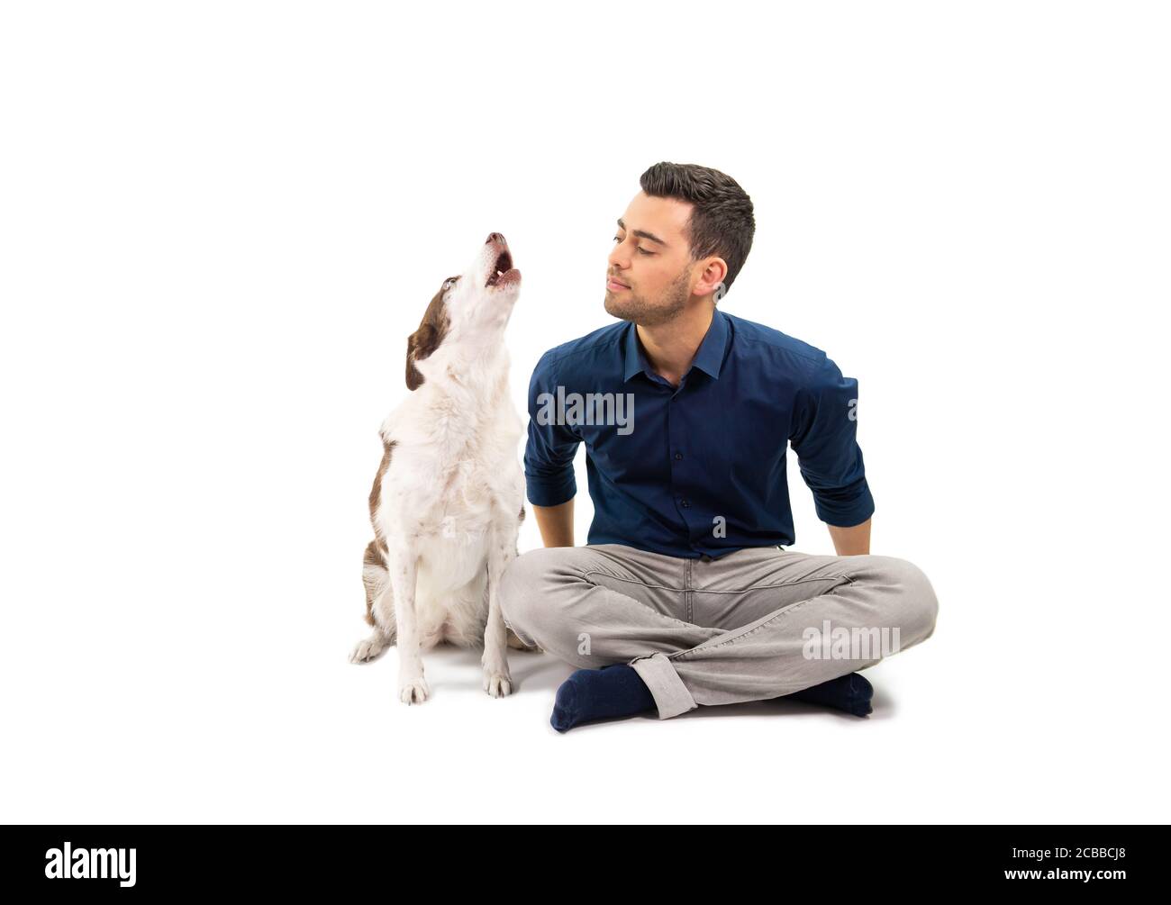Proprietario di animali domestici seduto sul pavimento con il suo cane urlante, isolato su bianco Foto Stock