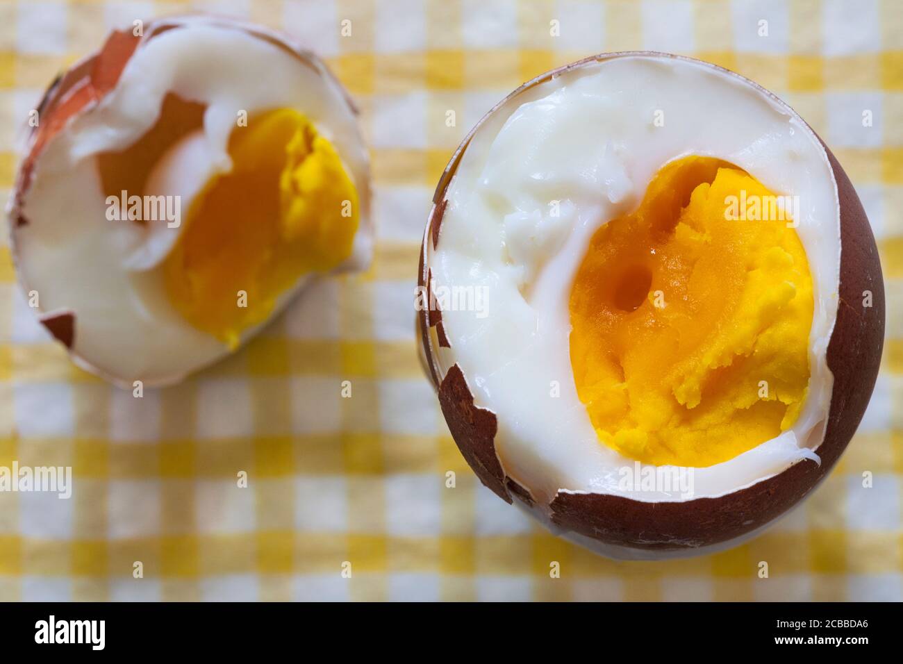 M&S British Farmed Free Range Maran Island Brown Egg on serviette di tovagliolo giallo e bianco - uovo bollito con taglio superiore per mostrare il tuorlo Foto Stock