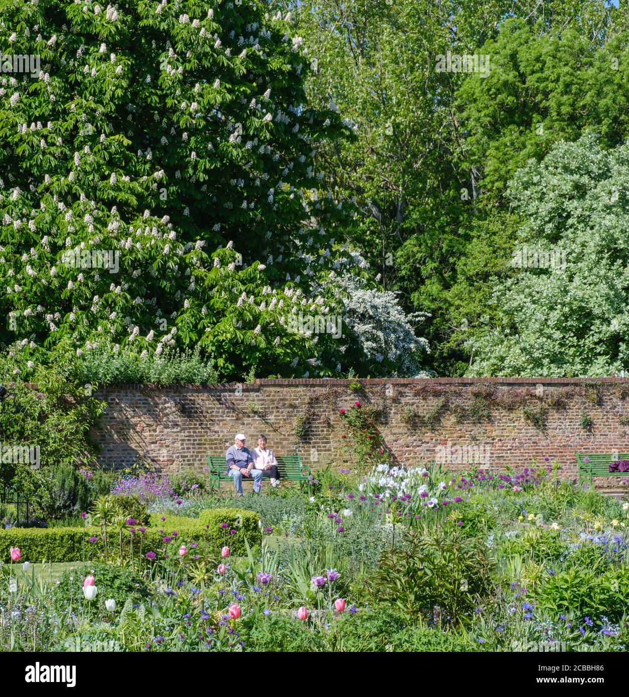 Una coppia anziana si siede su una panchina presso l'Eastcote House Walled Garden, tra tress e fiori. Hillingdon, Londra Foto Stock