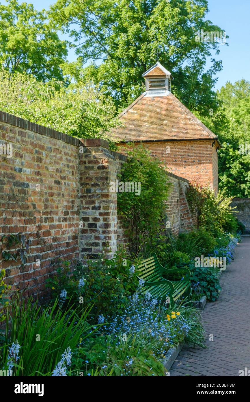 Panca vuota del parco con fiori e vecchio muro di mattoni. Grado II elencato 18 ° secolo Dovecote sullo sfondo. Eastcote Walled Garden, Hillingdon, Londra Foto Stock