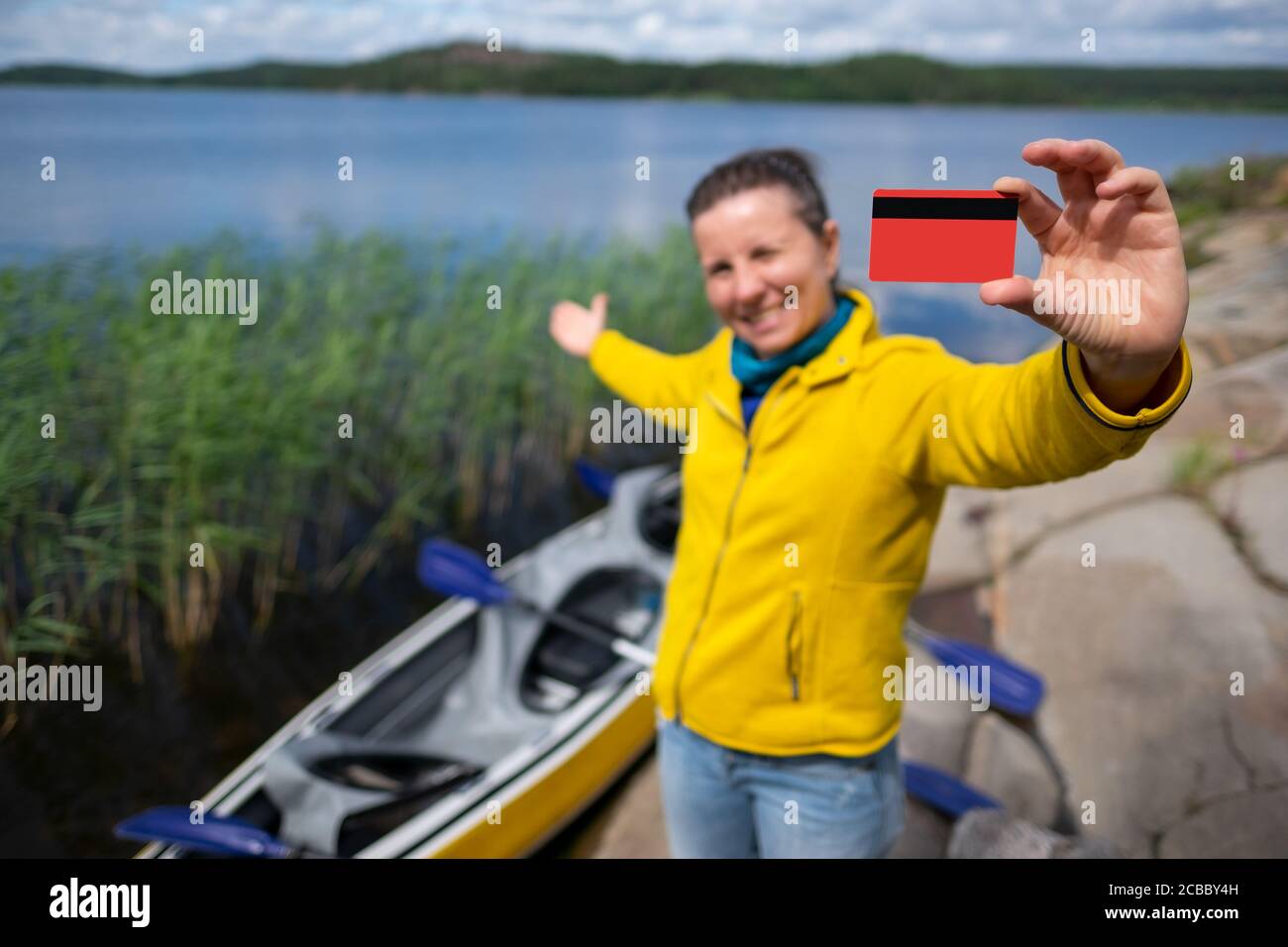 Giovane donna con una carta di credito che mostra lago e kayak. Foto Stock