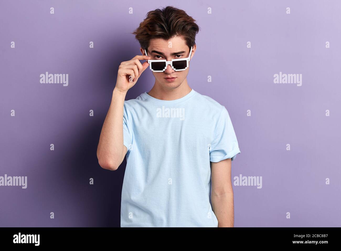 un uomo di moda sicuro che tocca gli occhiali da sole. guardando la fotocamera. stile di vita, tempo libero, tempo libero, sfondo blu isolato, scatto in studio Foto Stock