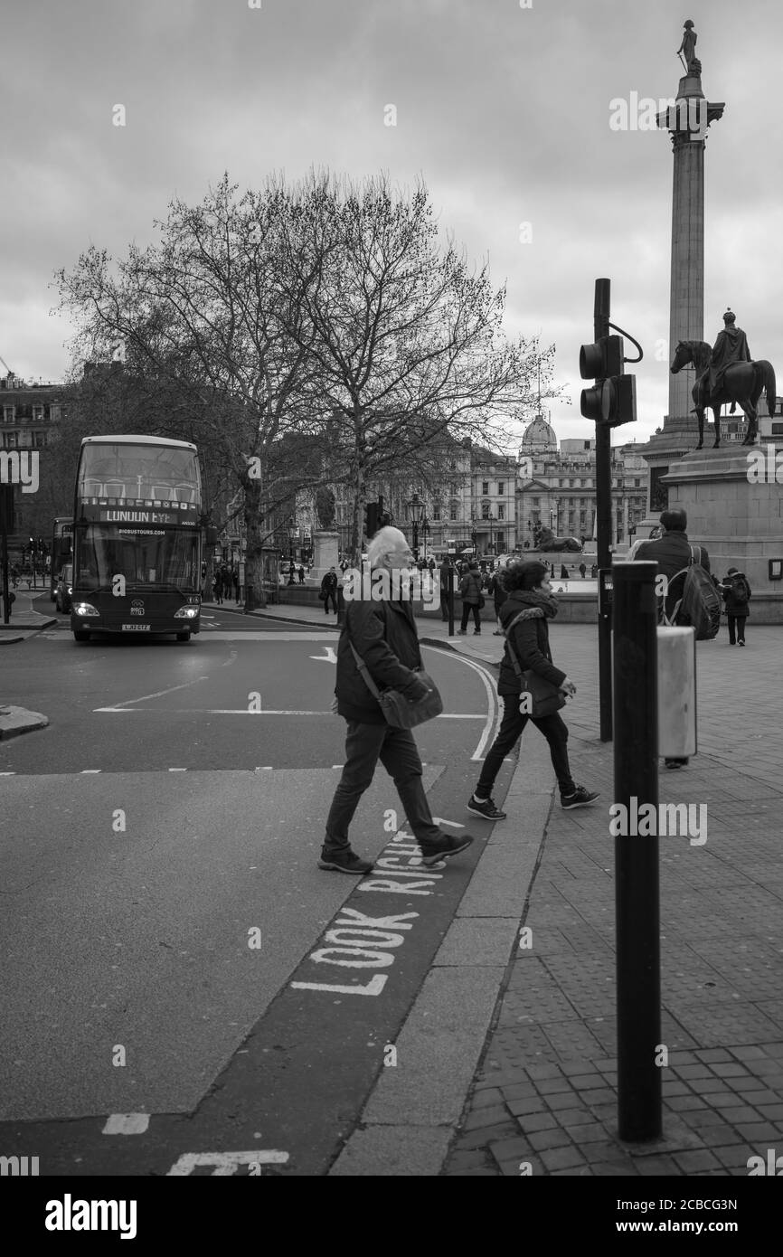 La gente ha visto attraversare la strada per Trafalgar Square Londra, con la colonna Nelsons e la statua come sfondo. Foto Stock