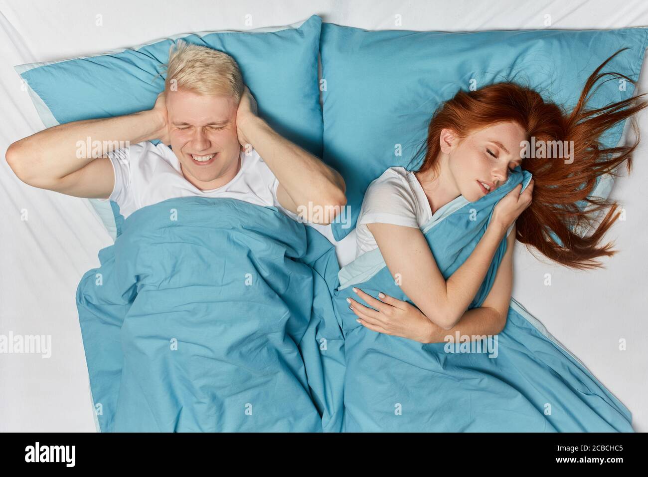 l'uomo serio infelice che giace con le braccia incrociate non può cadere asleeppy l'uomo biondo non vuole ascoltare il russare della moglie Foto Stock