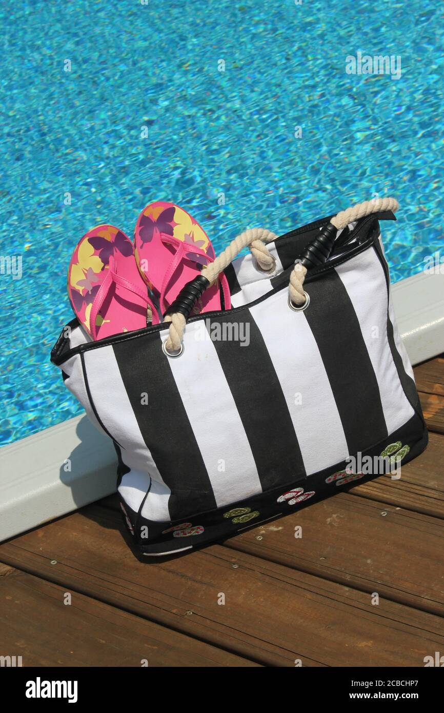 Borsa da spiaggia e accessori sul bordo di una piscina Foto Stock