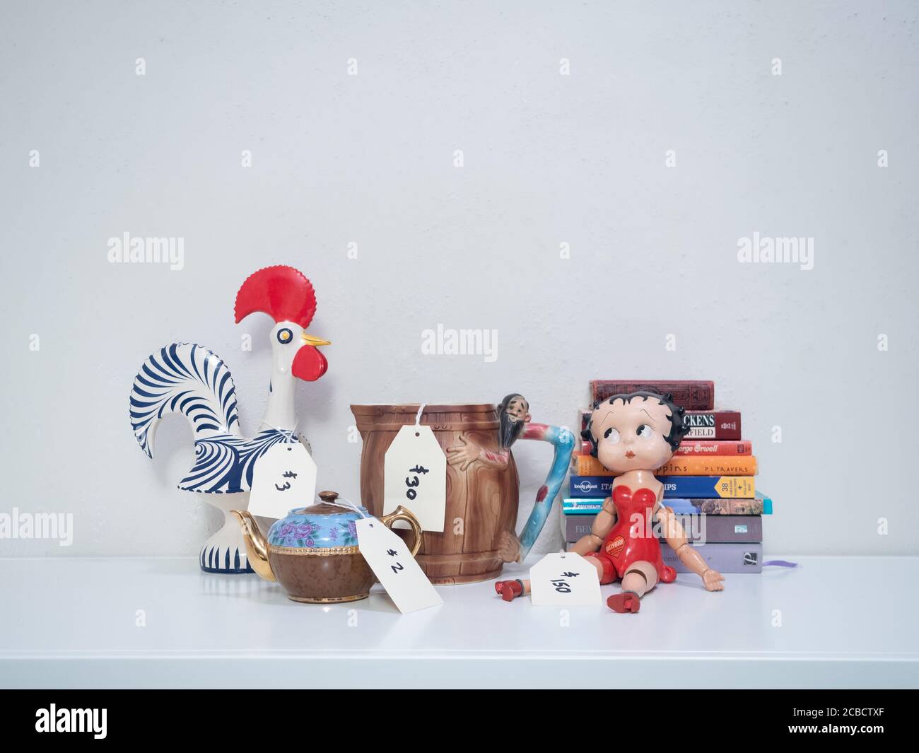 Prezzo caraffa, lampada, opere d'arte, bambola Betty Boop e teiera su un bancone bianco con sfondo bianco. L'immagine ha spazio per la copia. Foto Stock