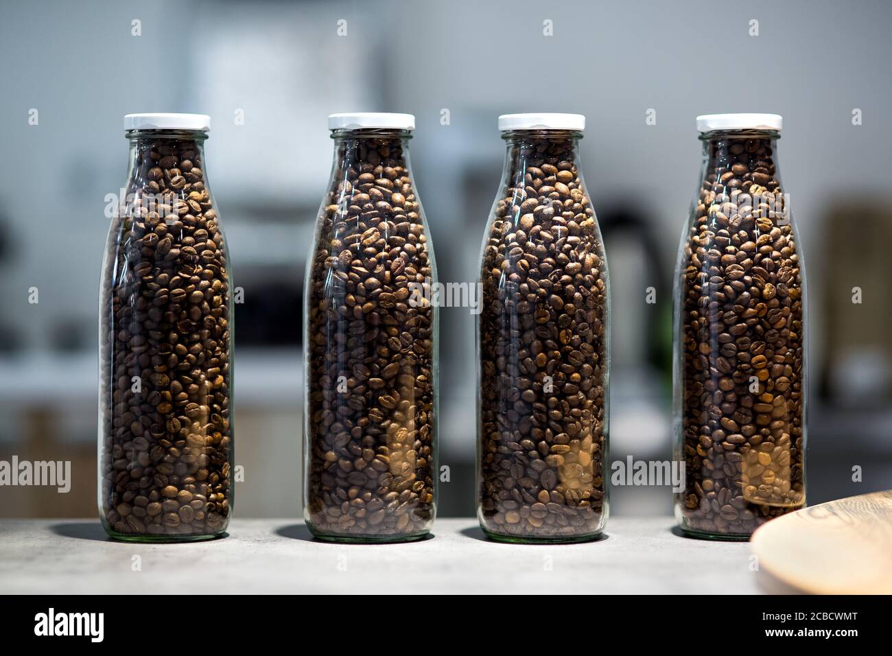 Bottiglie trasparenti in vetro riempite con chicchi di caffè tostati, contenitori trasparenti con coperchio bianco sul tavolo della matrina del negozio. Foto Stock