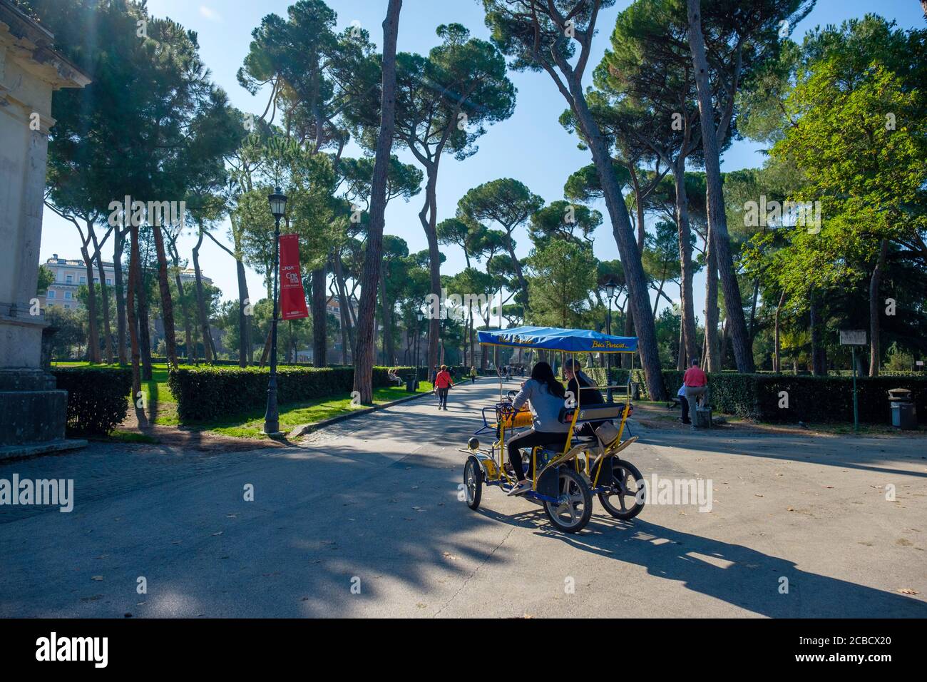 Persone che si godono una giornata estiva a cavallo di un Bici Pincio Rent a Bike Rental quadricycle, Villa Borghese Park, Roma, Italia Foto Stock