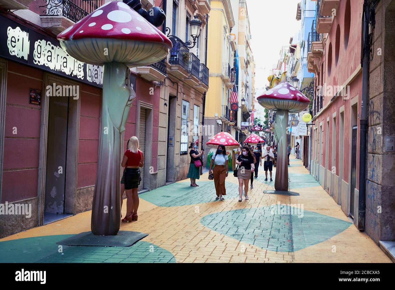 Sculture di funghi rossi e bianchi costeggiano la Calle San Francisco dipinta di giallo e verde ad Alicante, Spagna Foto Stock