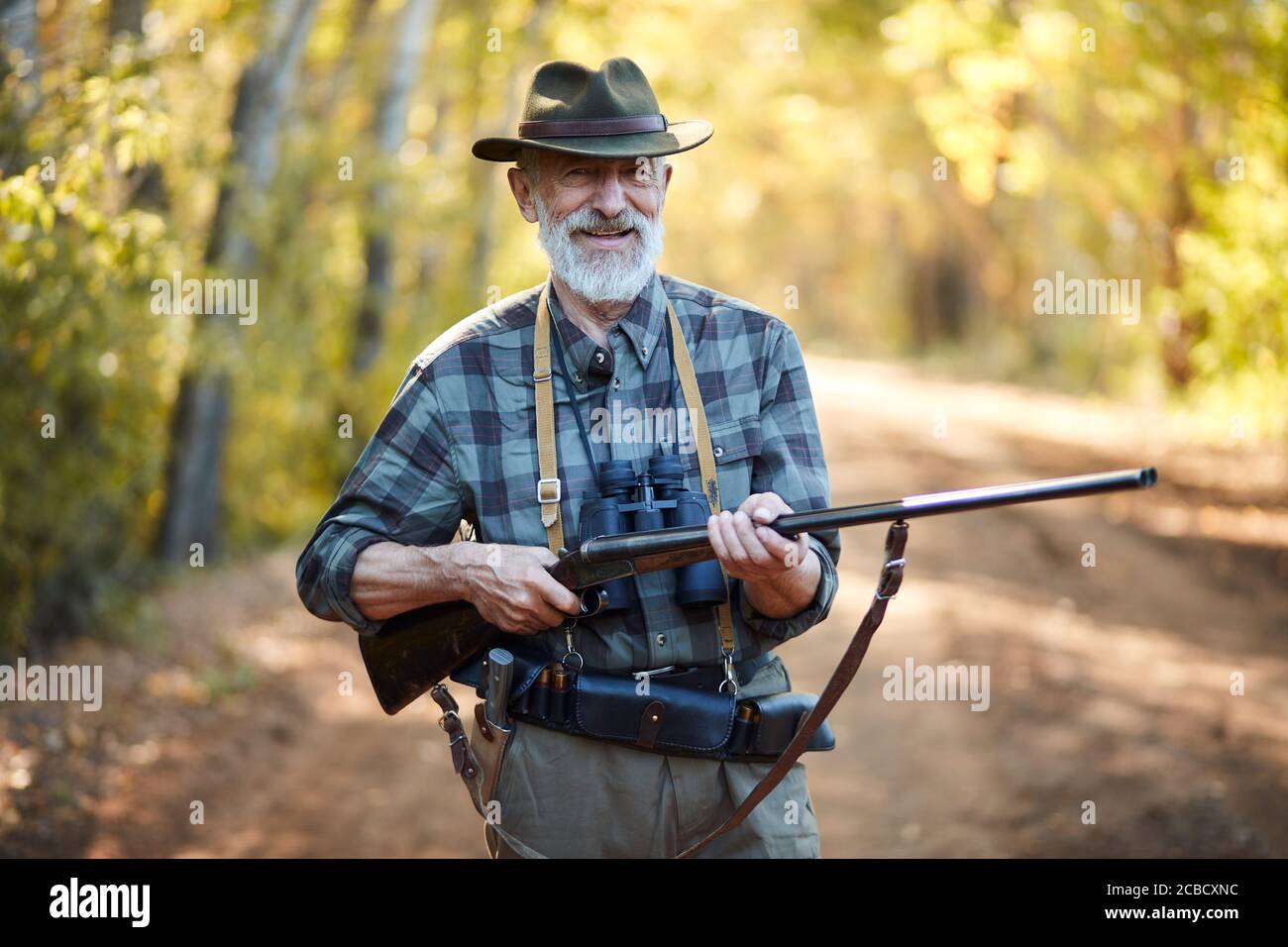 Ritratto di un cacciatore positivo che tiene la pistola, stare in foresta Foto Stock