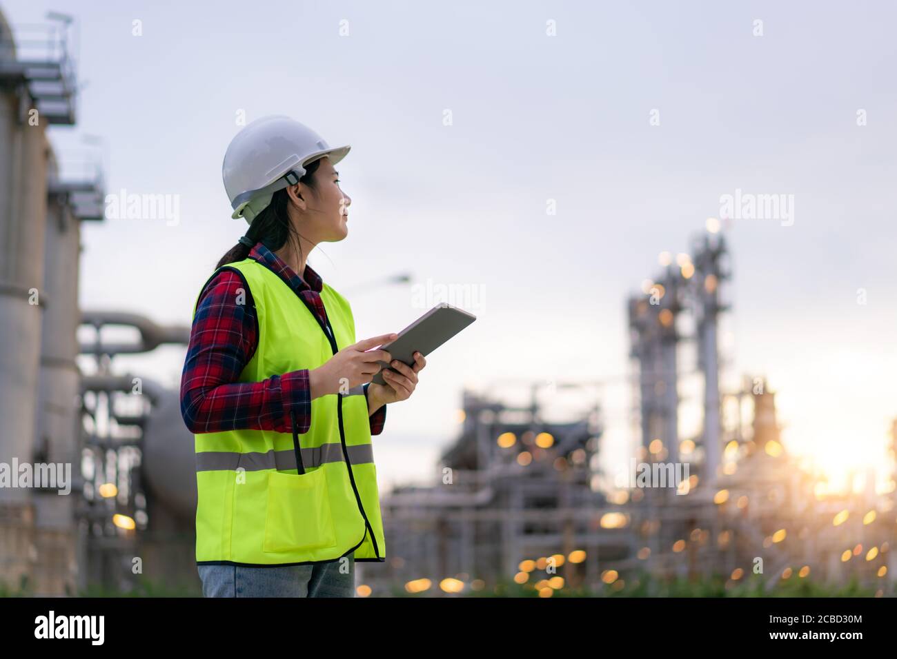 Donna asiatica ingegnere petrolchimico che lavora con tablet digitale all'interno di impianti di raffineria di petrolio e gas fabbrica per il controllo di qualità di sicurezza ispettore Foto Stock