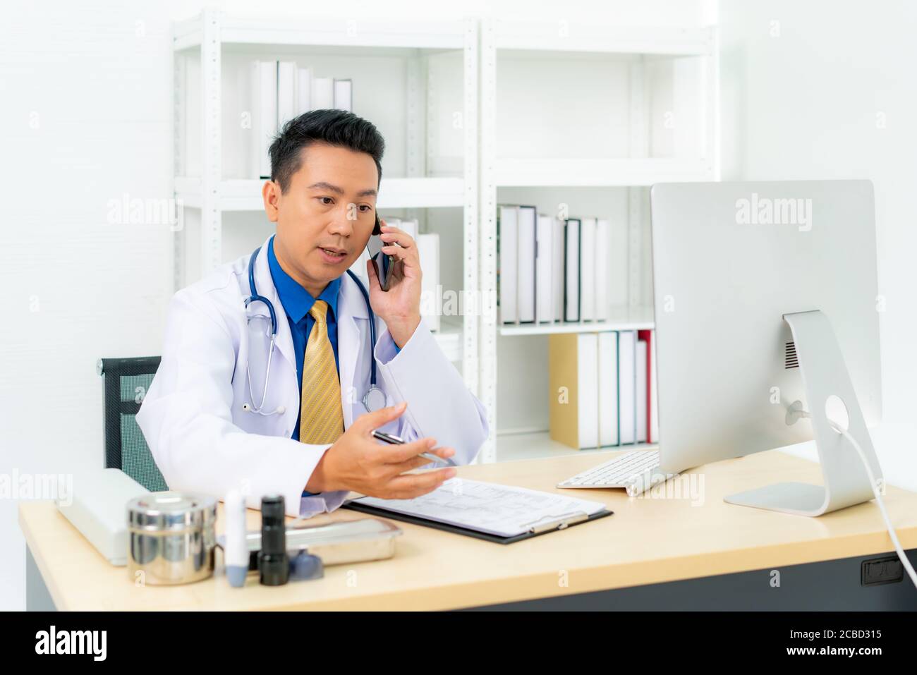 Asiatico uomo medico scrittura documento bianco parlare con il paziente di consulenza per telefono o telefono cellulare. Telemedicina, concetto di telesanità. Foto Stock