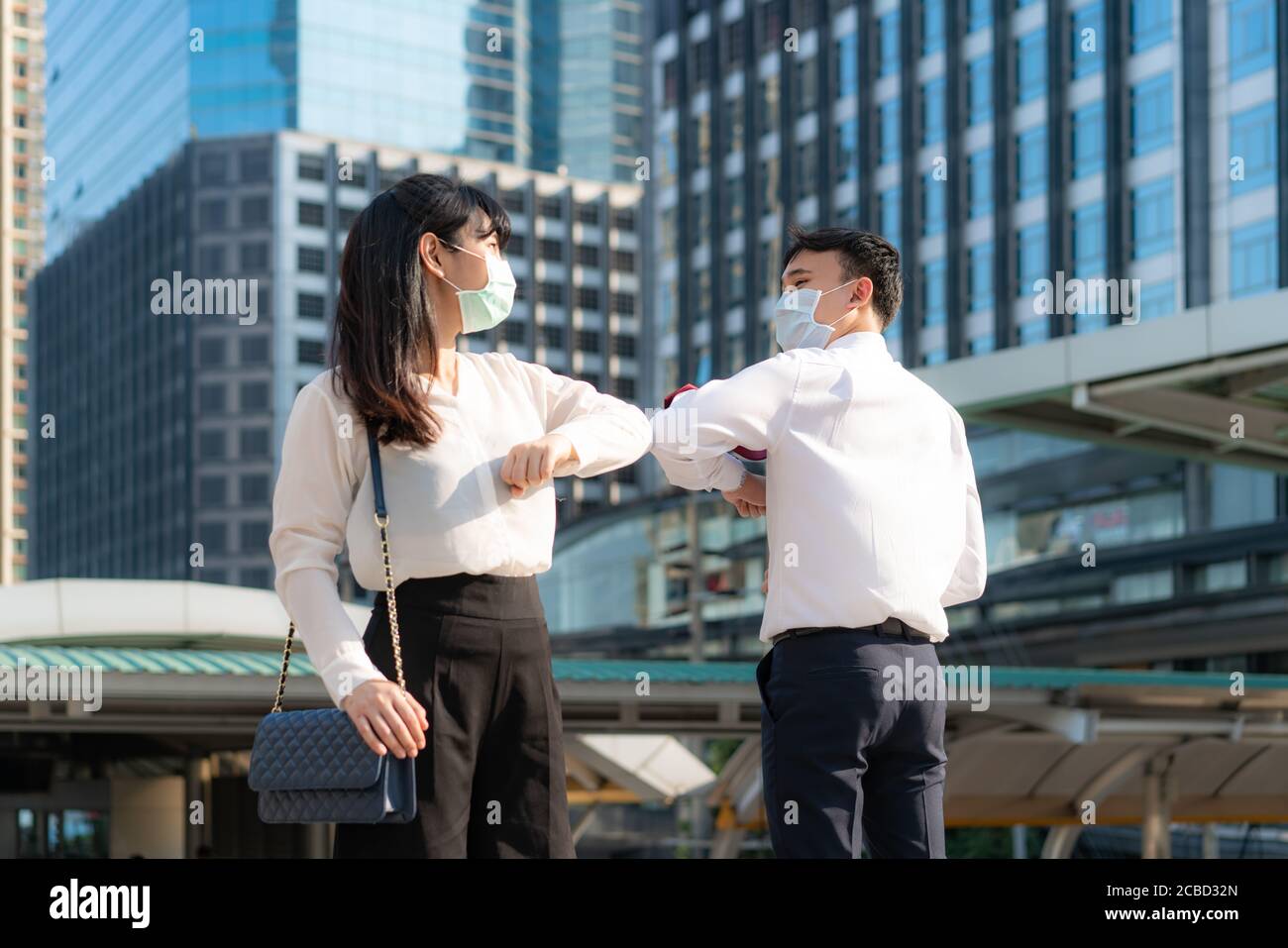 Gomito bump è nuovo saluto per evitare la diffusione di coronavirus. Due amici d'affari asiatici si incontrano di fronte all'edificio degli uffici. Invece di salutare Foto Stock