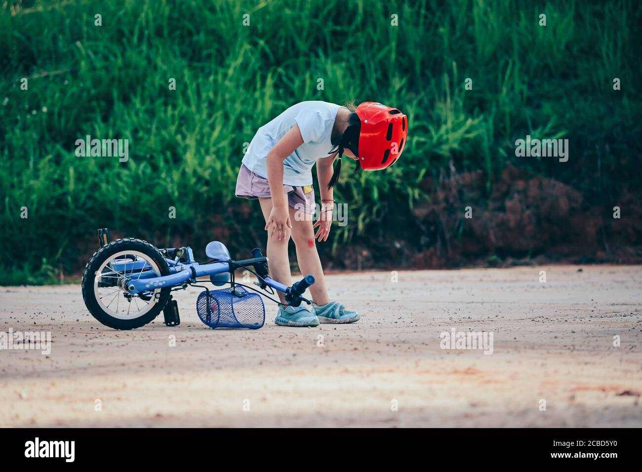 bambina che cade dalla bicicletta all'aperto bambino che indossa casco da bici. Sport di sicurezza per il tempo libero con concetto di bambini Foto Stock
