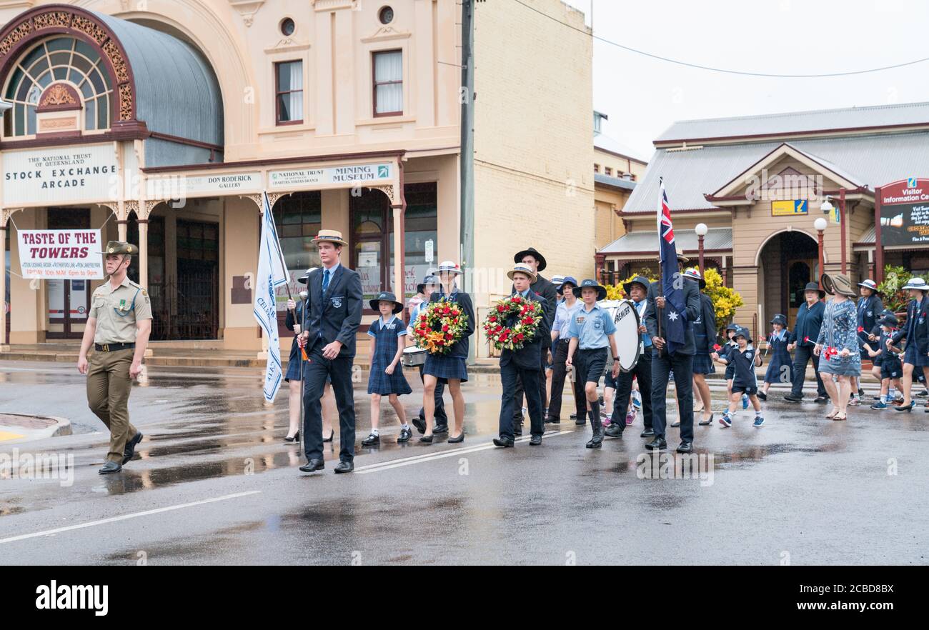 Charters Towers, Australia - 25 aprile 2019: I bambini della scuola che marciano sotto la pioggia il giorno di Anzac portando le corone e i papaveri Foto Stock