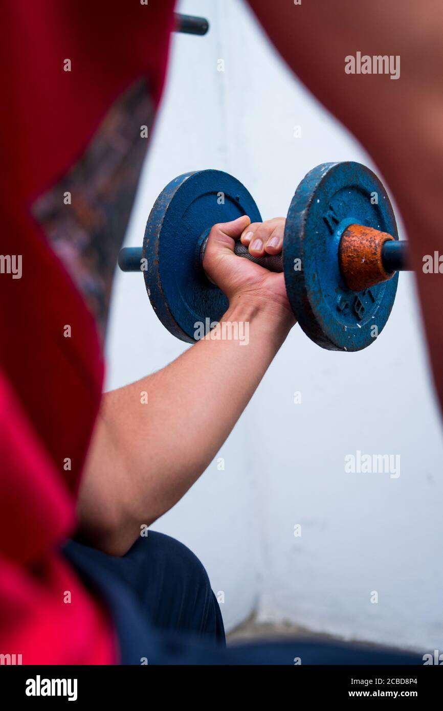Giovane uomo che solleva i pesi blu della vecchia palestra sul pavimento in palestra Foto Stock