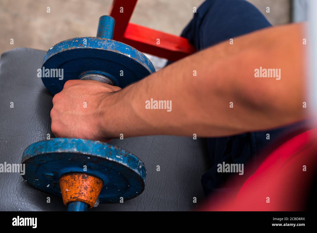 Giovane uomo che solleva i pesi blu della vecchia palestra sul pavimento in palestra Foto Stock