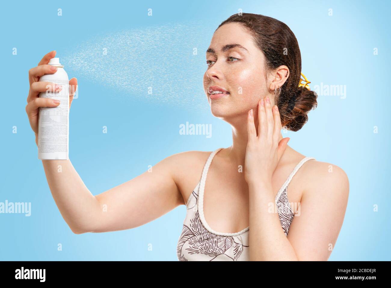 Una giovane donna caucasica con pelle bagnata spruzzi acqua termale sul viso. Sfondo blu. Concetto di cosmetologia, cura della pelle e idratazione. Foto Stock