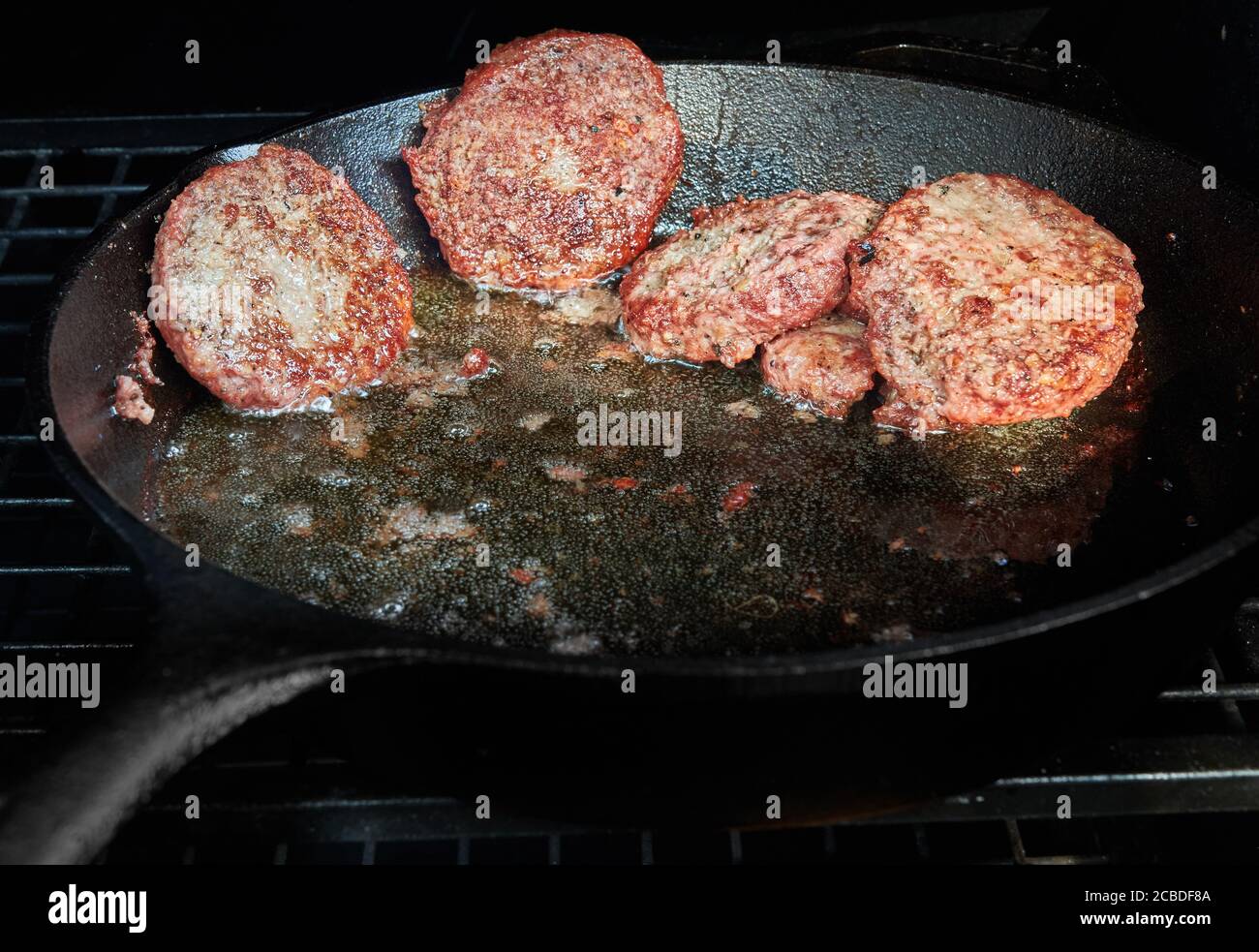 Hamburger di manzo cotti in una padella di ghisa su un barbecue al carbone. Foto Stock