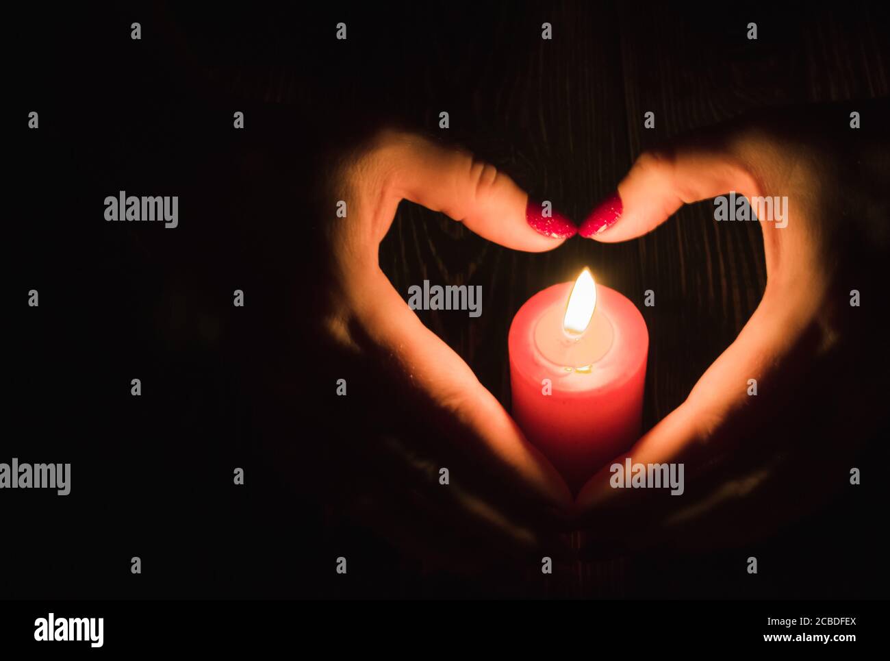 A forma di cuore mani femminili intorno a bruciare candela rossa Foto Stock