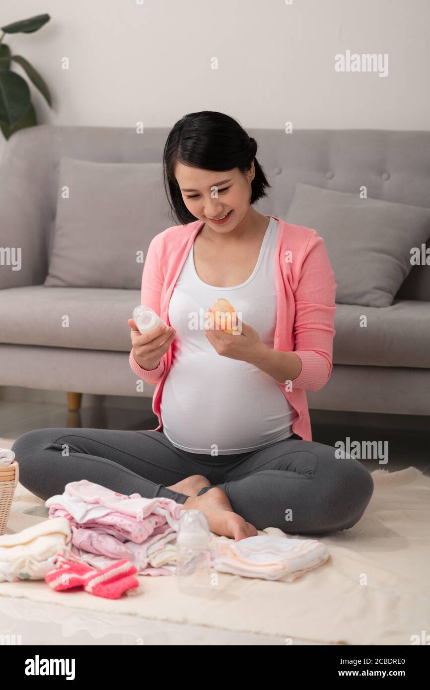 bella donna asiatica incinta usando la lista di scrittura della penna sul notebook imballaggio e preparazione dei vestiti del bambino nel cestino Foto Stock