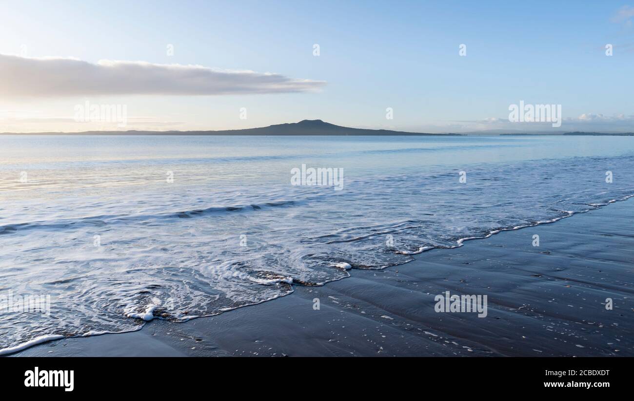 Spiaggia di Milford all'alba con onde di turbolenza in primo piano E Rangitoto Island in lontananza Foto Stock