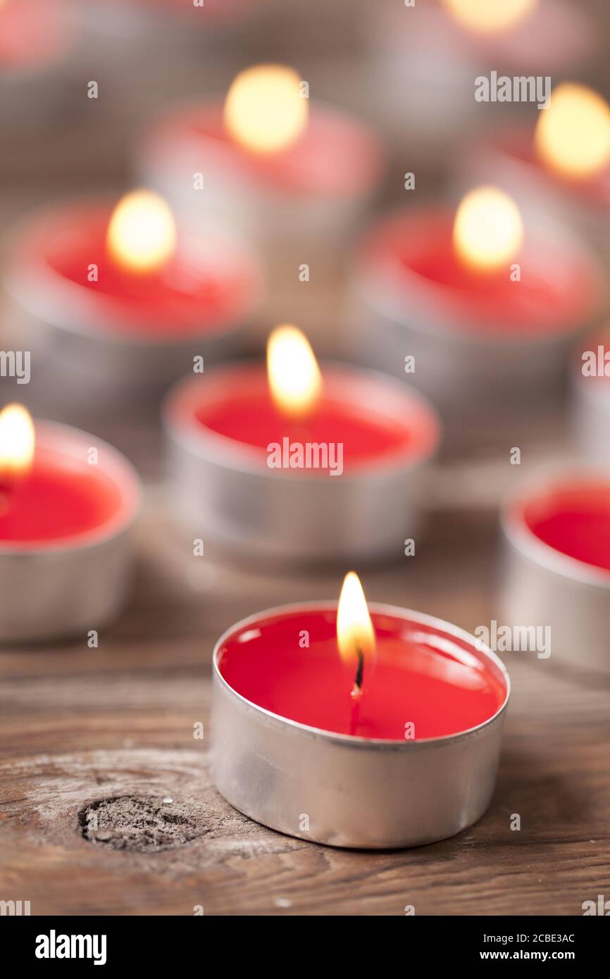 Colpo verticale di candele di tè rosse e illuminate su un superficie in legno Foto Stock