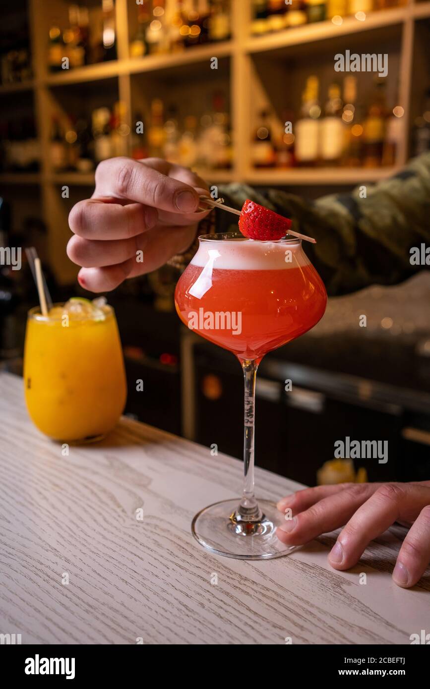 bevande alcoliche, persone e concetto di lusso - barista con bicchiere e scorza di limone preparazione cocktail al bar Foto Stock
