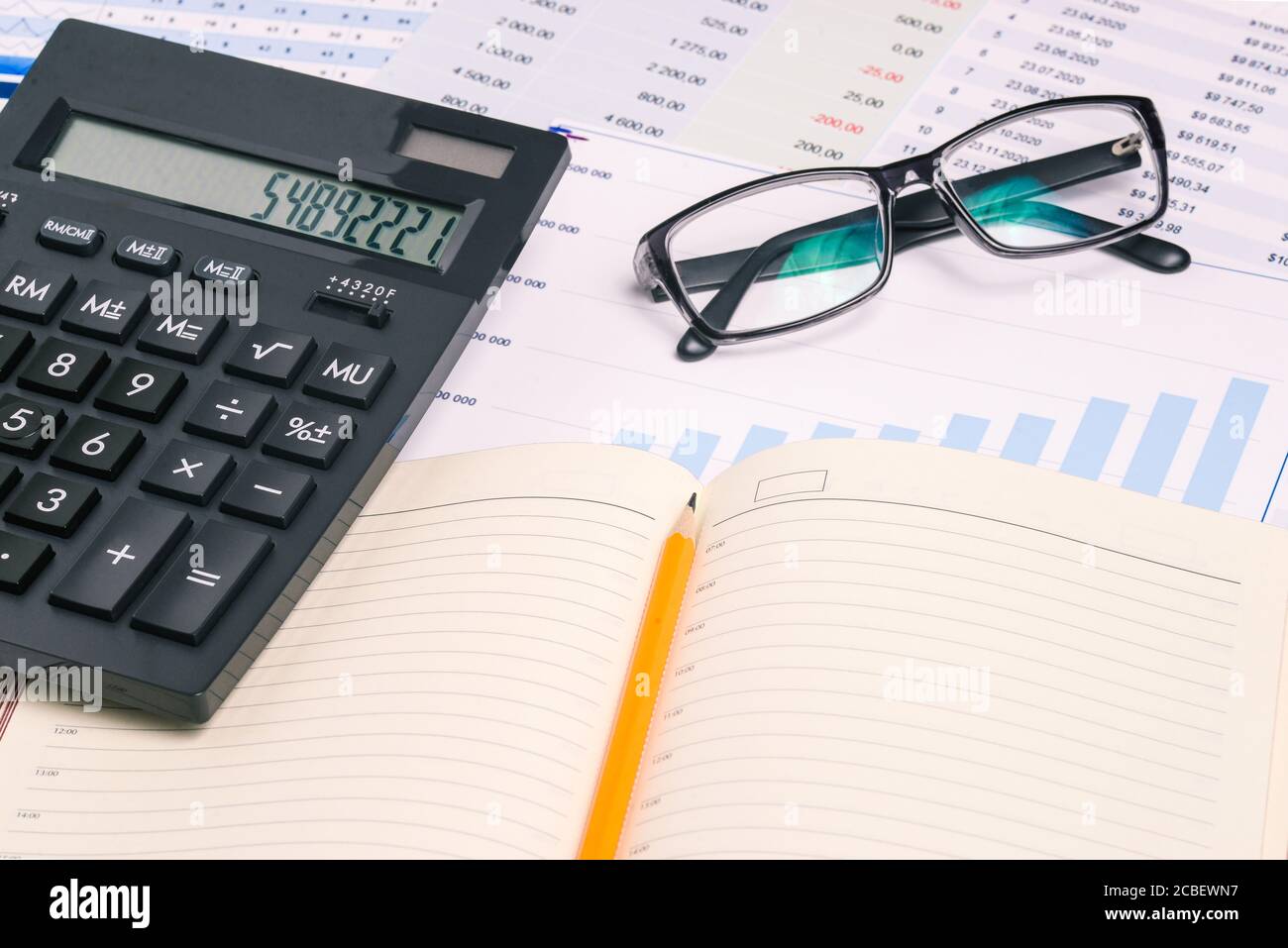 Diario, occhiali e calcolatrice sulla scrivania dell'ufficio. Desktop dell'uomo d'affari con grafici e numeri. Contabilità, consulenza e analisi di marketing. Foto Stock