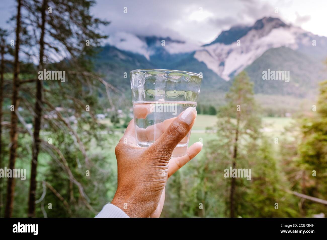 bicchiere d'acqua in mano che si affaccia sulle montagne, acqua potabile Foto Stock