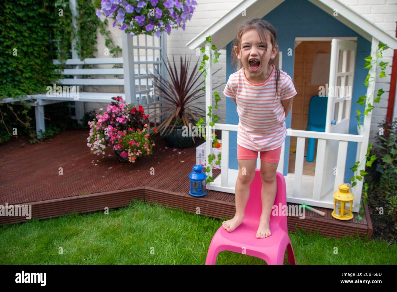 La bambina bianca di quattro anni si trovava su una sedia di plastica rosa per bambini che urla di fronte a una casa Wendy bianca e blu. Inghilterra Regno Unito Foto Stock