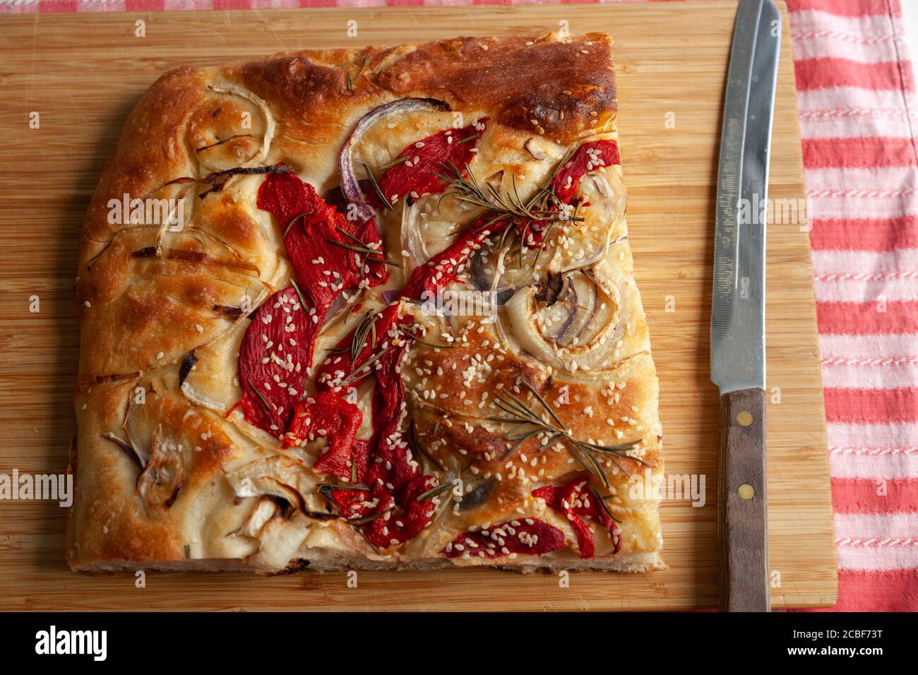 Un grande pezzo di focacia appena sfornata con peperoni rossi, cipolle, semi di sesamo e rosmarino Foto Stock