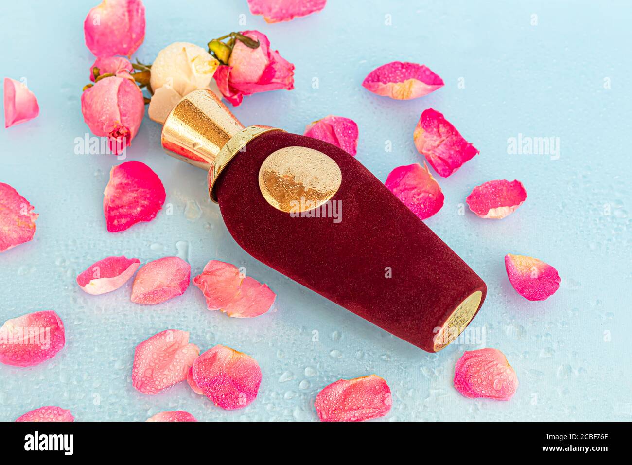 Bottiglia di velluto con profumo da donna. Circondato da petali di rosa su uno sfondo chiaro. Spazio di copia Foto Stock