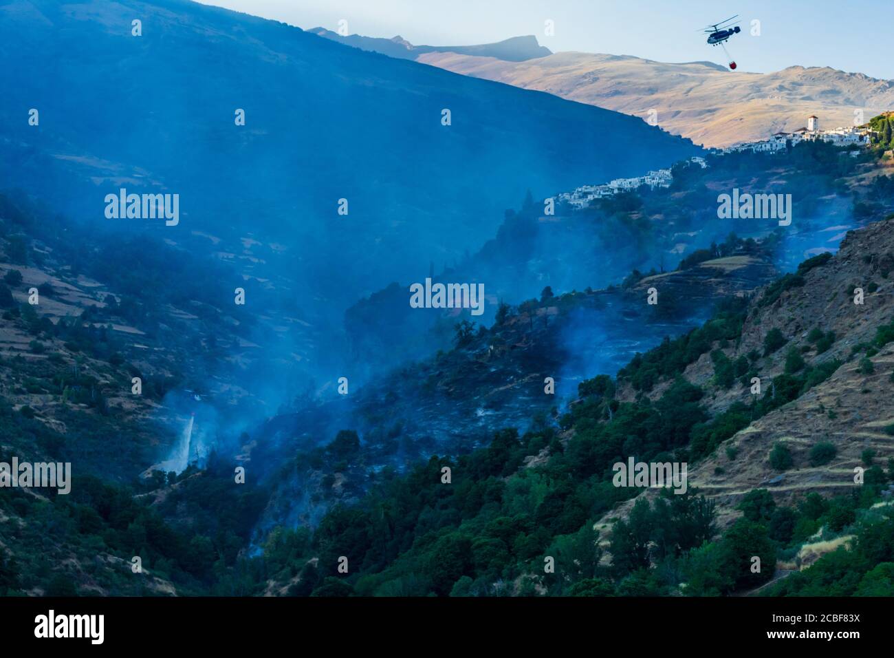 Elicottero con un sacco d'acqua che lavora per spegnere un incendio a Las Alpujarras de Granada. Foto Stock