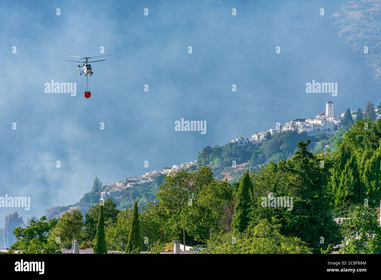 Elicottero con un sacco d'acqua che lavora per spegnere un incendio a Las Alpujarras de Granada. Foto Stock