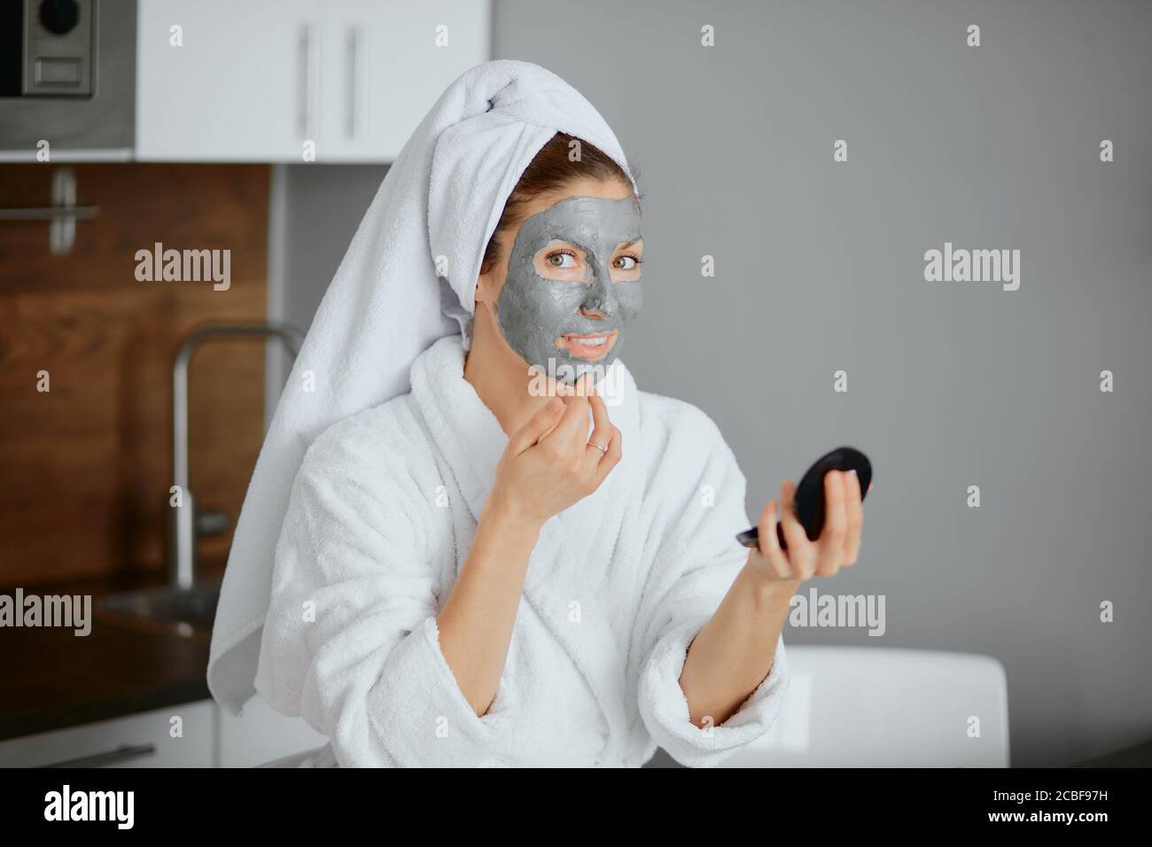 bella donna in accappatoio e asciugamano seduta con maschera viso in camera da letto. procedure di bellezza a casa Foto Stock