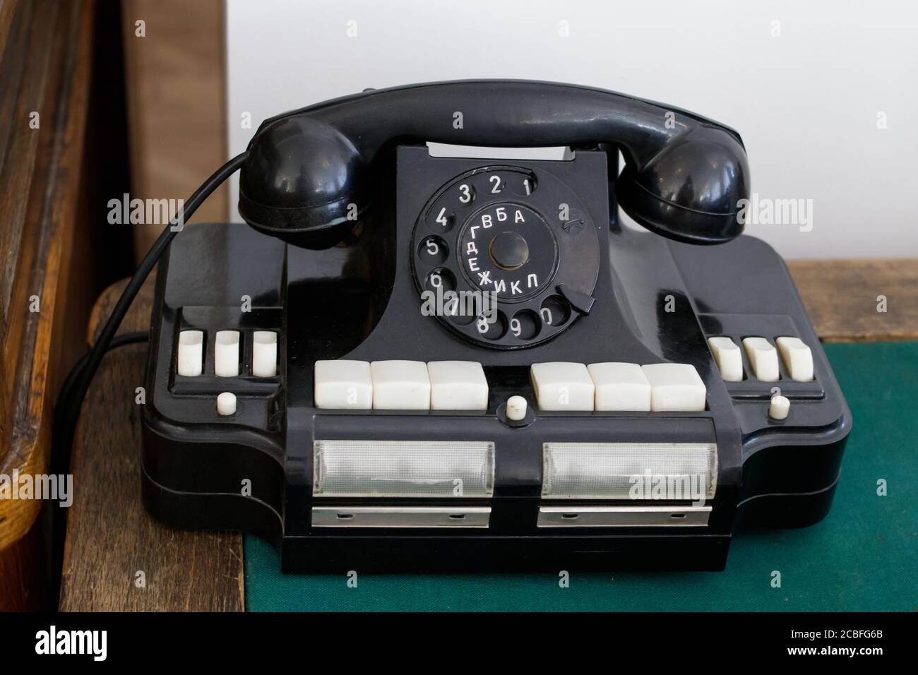 Vecchio telefono da ufficio sovietico con lettere russe su un tavolo di legno, il piano portapaziente è coperto di tessuto verde. Foto Stock