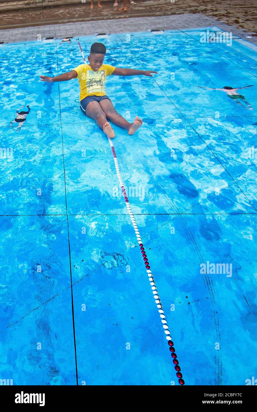 Un ragazzo gioca su un'installazione d'arte temporanea raffigurante una piscina durante il tempo caldo nel centro di Londra. Foto Stock