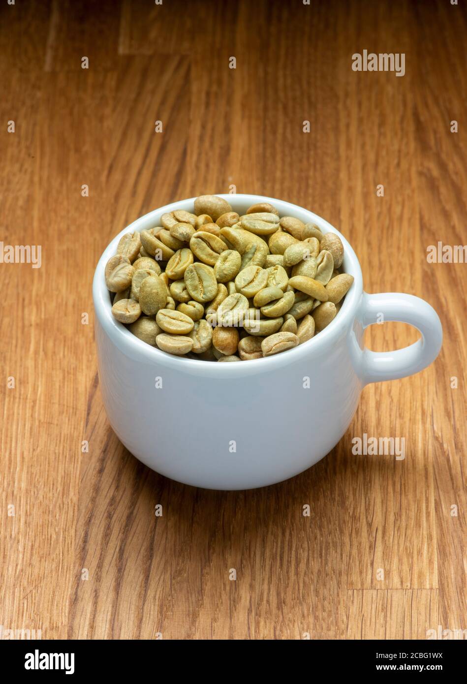 Chicchi di caffè verdi in una tazza da caffè bianca. Stato grezzo prima della tostatura. Foto Stock