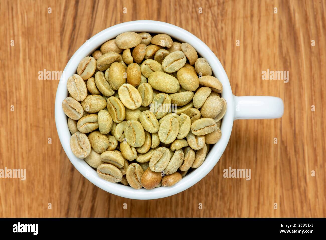 Chicchi di caffè verdi in una tazza da caffè bianca. Stato grezzo prima della tostatura. Foto Stock