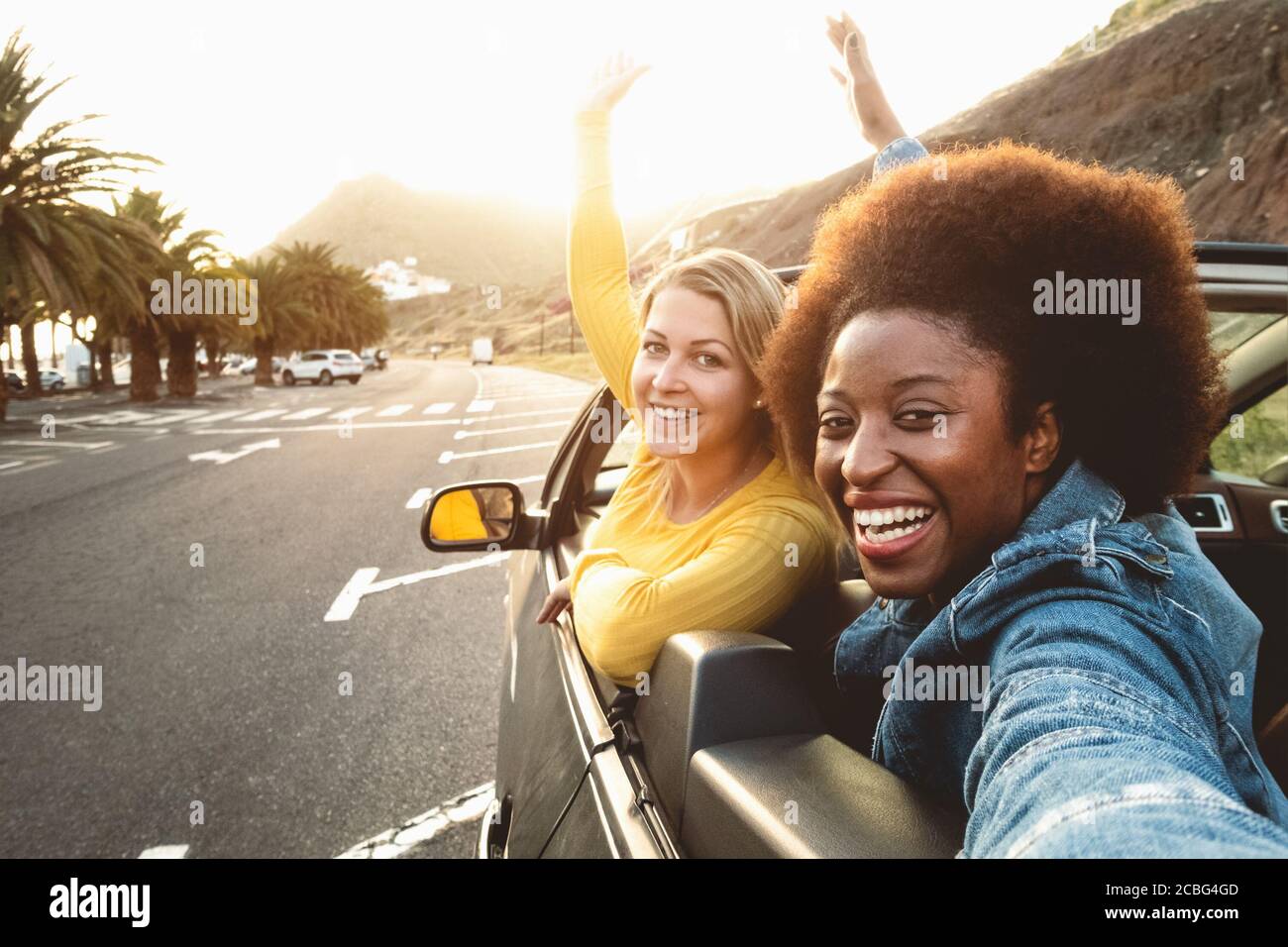 Giovani donne felici che prendono selfie facendo viaggio su strada - Viaggi ragazze che si divertono a guidare in un'auto convertibile alla moda scoprendo nuove luoghi Foto Stock