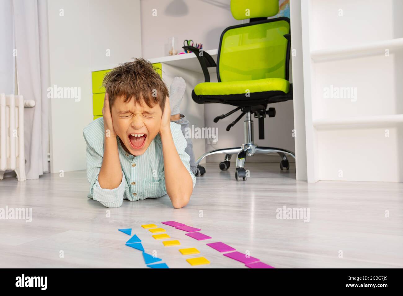 Ragazzo autistico con sviluppo educativo esercizio forma geometrica urlo copertura orecchie e posare sul pavimento Foto Stock