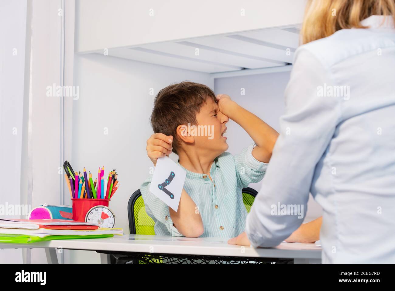 Il ragazzo con disturbo autistico dello spettro mostra dolore ed espressione negativa mentre imparando i numeri seduti dall'insegnante Foto Stock