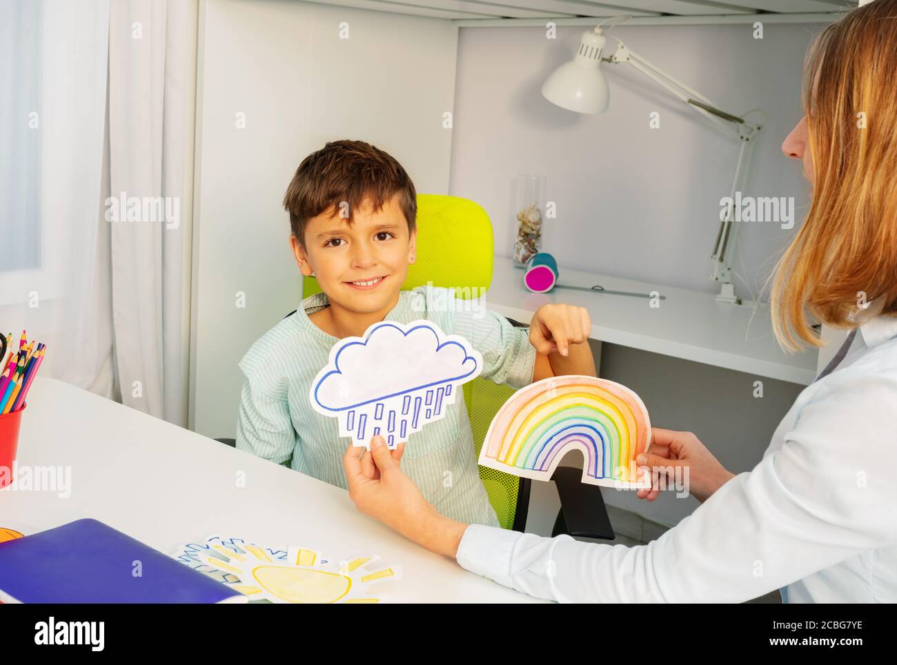 Bambino durante la terapia di sviluppo di aba che si siede selezionando fra due carte di arcobaleno e tempesta Foto Stock