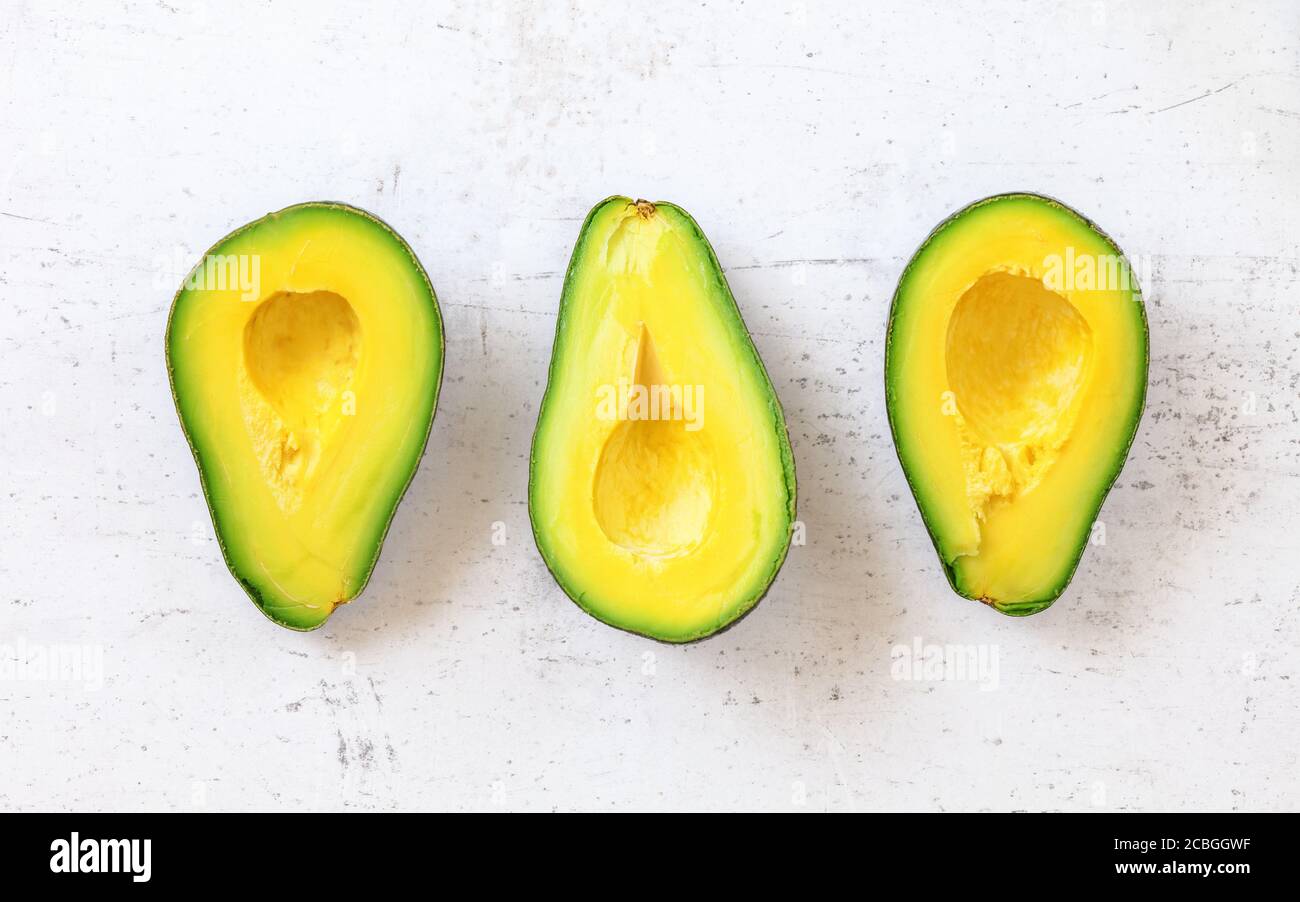 Vista dall'alto verso il basso, tre metà di avocado su tavola da lavoro bianca. Foto Stock