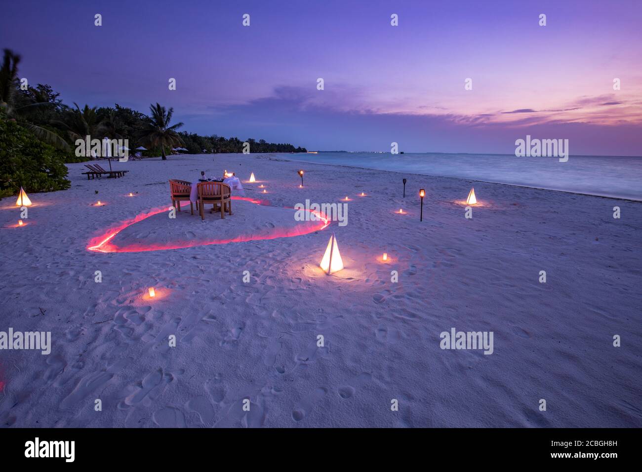 Una giovane coppia condivide una cena romantica con il cuore delle candele sulla spiaggia di sabbia del mare. Cena romantica al tramonto con candele cuore sulla spiaggia di sabbia del mare cielo Foto Stock