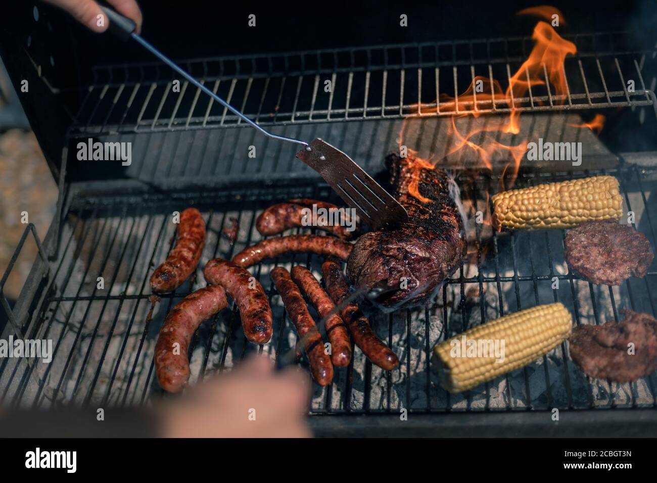 Uomo che cucina su barbecue, bistecca argentina, salsicce, carne e mais in un barbecue in una calda giornata estiva Foto Stock